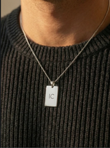 שרשרת לגבר עם תליון מתכתי דוגמת תג צבא על צוואר גבר בחולצה שחורה פתוחה