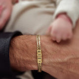 צמיד זהב עם חריטה אישית של שמות BEN, AYA, EMMA, LIV על פרק כף יד של גבר לצד יד תינוק